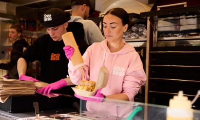 A worker squeezes sauce on to a filled jacket potato in a tray