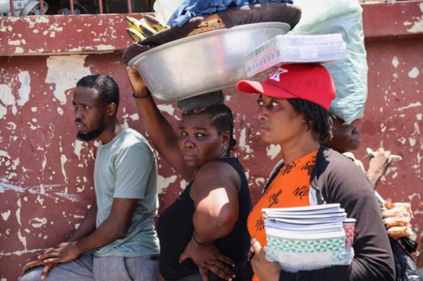 People on the streets of Port-au-Prince. One woman has a large me<em></em>tal co<em></em>ntainer n her head filled with belongings. Another is balacing two books on her head and carryying more in her arm