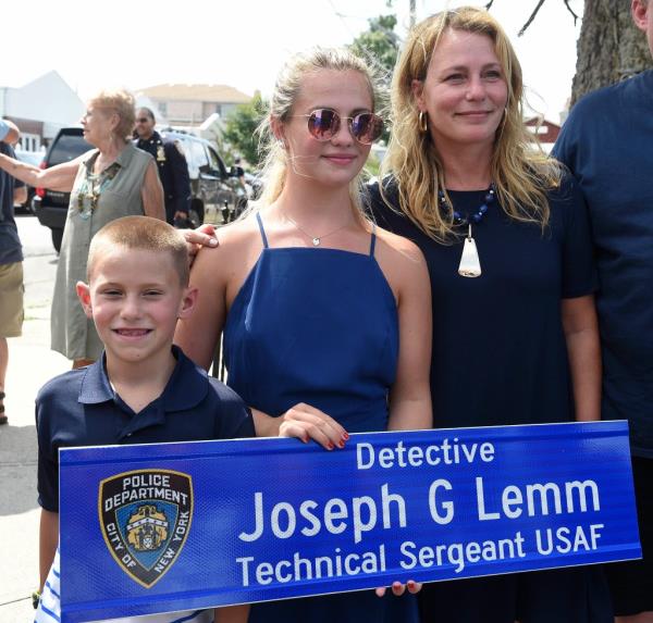 Photo shows family holding a blue street sign that says Detective Joseph G. Lemm, Technical Sergeant USAF.