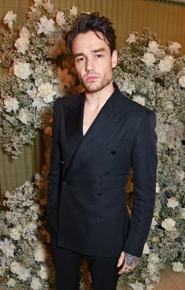 Liam Payne in a black suit standing in front of white flowers.