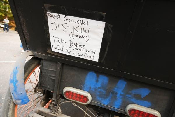 Photo of the handwritten sign on the back of Mactor Sarr's pedicab that reads, “Israel’s Genocide / 31K Killed (murdered) / 13K Babies Murdered - Starved / funded by U.S.A (You)."