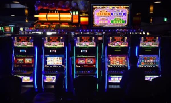 A man, co<em></em>ncealed in shadow, sits at a poker machine 