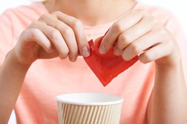 A woman tearing open a packet of artificial sweetener