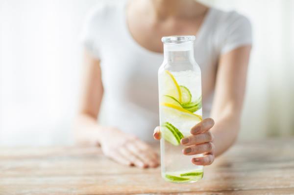 A woman holding a water bottle with lemon and cucumber