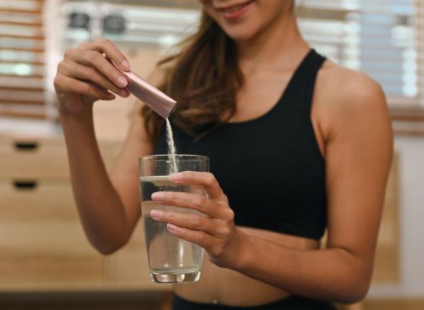 A woman pours a packet of flavoring into a glass of water