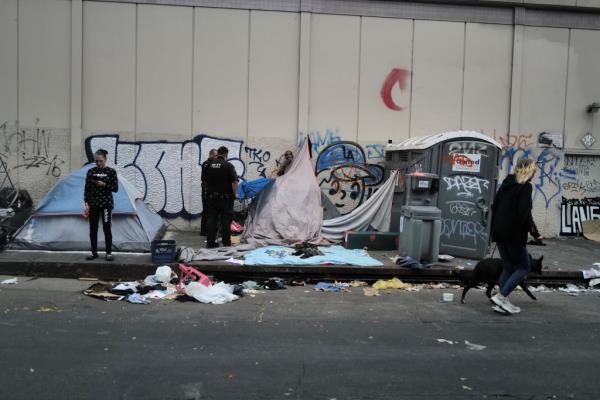 A group of people, including Sue Wicks and Dustin Poirier, near a graffiti-covered wall in Skid Row, downtown Los Angeles, known for its homelessness and drug use.