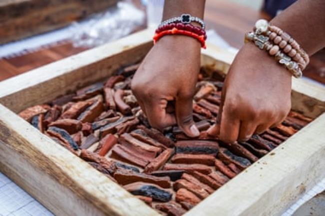 A pair of hands presses pottery shards into cement co<em></em>ntained within a square wooden f<em></em>rame